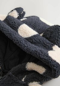 Sort og beige fuzzy hætte med små rundede ører, der viser blødt tekstureret stof og sort inderside.