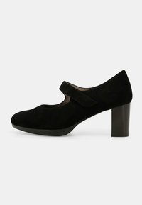 Scarpa con tacco in suede nero, con punta arrotondata e una fascia in Velcro sul collo del piede. Il tacco è di tipo blocco e alto circa 7 cm.