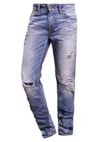 Světle modré džíny z denimu s úzkým střihem, které mají oprané části, třásně na lemech a kontrastní švy. Navrženy s pěti kapsami.