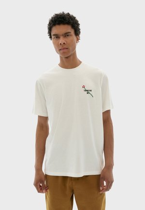 T-shirt en coton blanc avec un petit motif floral et du texte, col rond, manches courtes et coupe décontractée. Les accents incluent de la broderie.