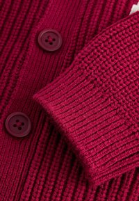 Teksturowany sweter kardigan w głębokim magencie, z prążkowanym wzorem, dwoma dużymi fioletowymi guzikami oraz mankietami o dopasowanym kroju.
