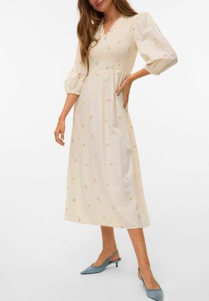 Cremefarbenes Midikleid mit Puffärmeln, gerüschtem Oberteil und floralen Stickereien in Pastelltönen. Mit seitlichen Taschen und einem V-Ausschnitt.