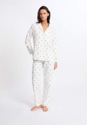 Conjunto de pijama de algodón blanco que incluye una camisa con botones y pantalones a juego. Ambas piezas están decoradas con pequeños patrones de corazones en varios colores.