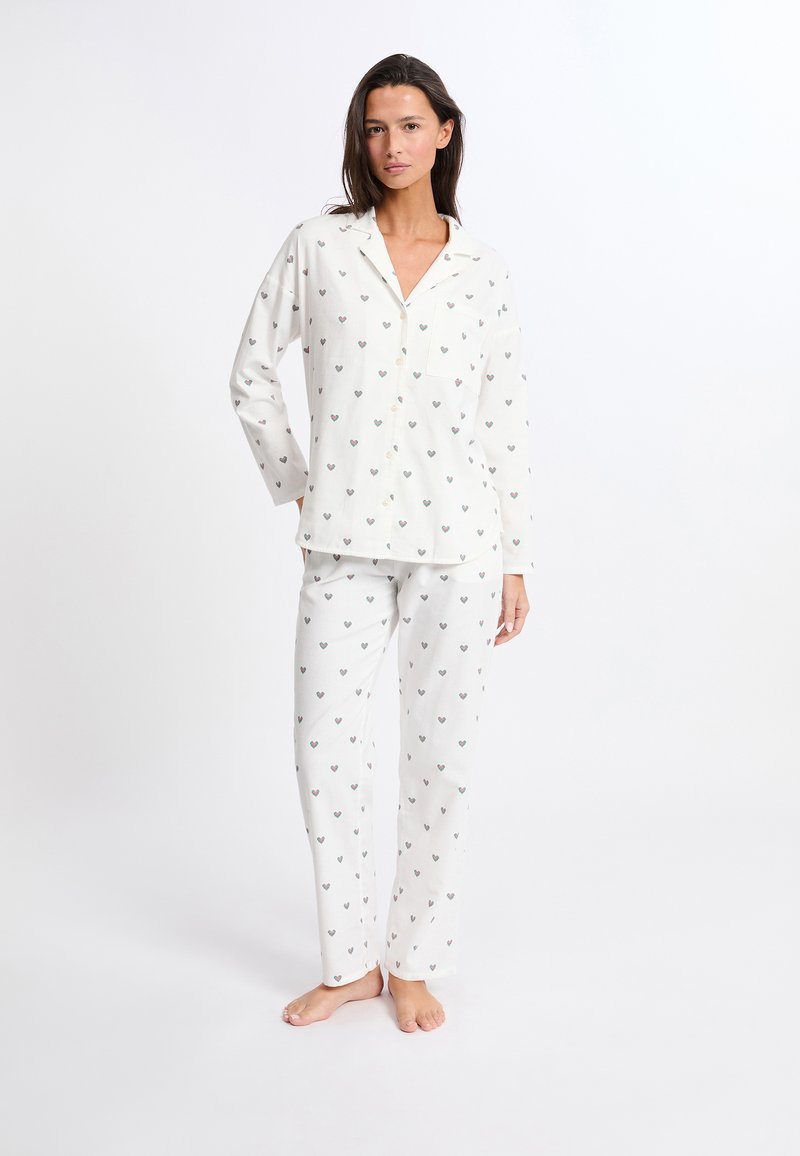 Weißes Baumwoll-Schlafanzug-Set mit einem knöpfbaren Oberteil und passenden Hosen. Beide Teile sind mit kleinen Herzmustern in verschiedenen Farben geschmückt.