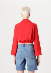 Blouse rouge cropped à manches longues et taille élastique, associée à un short en denim bleu avec deux poches arrière.