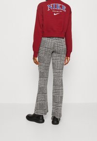 Burgundy kort sweatshirt med "NIKE"-logotypen och svarta utsvängda byxor med en strukturerad houndstooth-mönster. Svartskor fulländar outfiten.