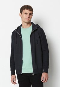 Dark navy zip-up hoodie with a front pocket, ribbed cuffs. Worn over a light mint t-shirt, showcasing a simple, casual design.