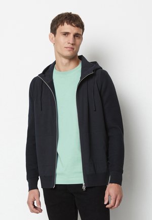 Dark navy zip-up hoodie with a front pocket, ribbed cuffs. Worn over a light mint t-shirt, showcasing a simple, casual design.