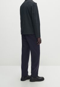 Giacca nera con una vestibilità rilassata, tessuto testurizzato e un sottile dettaglio di cucitura, abbinata a pantaloni blu navy e stivaletti neri.