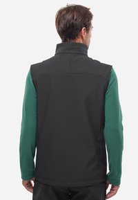 Schwarze ärmellose Jacke mit hohem Kragen und glatter Oberfläche, kombiniert mit einem langärmeligen grünen Hemd, das darunter sichtbar ist.
