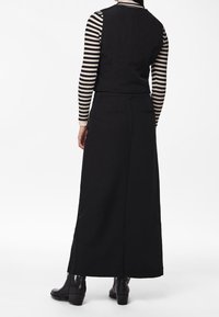 Schwarzer Rock mit langer Silhouette und einem Schlitz hinten, kombiniert mit einem gestreiften Langarmshirt. Stylisch mit Stiefeln bis zum Knöchel für einen eleganten Look.