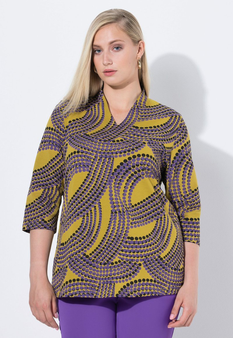 Driekwartmouwen blouse in mosterdgeel met golvende paarse en zwarte stippenpatronen. V-hals ontwerp met een soepele textuur.