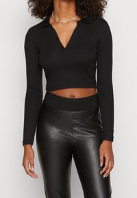 Schwarzes langärmliges Cropped-Top mit Kragen und V-Ausschnitt, kombiniert mit hochgeschnittenen schwarzen Kunstlederhosen mit strukturiertem Taillenbund.