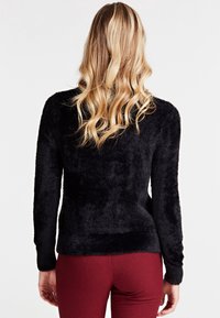 Pull noir et pelucheux à manches longues avec une coupe ajustée, associé à un pantalon à carreaux rouges. Le tissu semble doux et texturé.