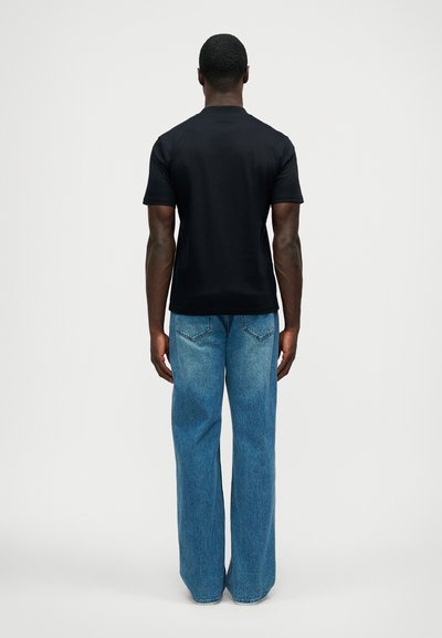 Μαύρο κοντομάνικο μπλουζάκι με στρογγυλή λαιμόκοψη, συνδυασμένο με ανοιχτό μπλε φαρδύ τζιν παντελόνι, σε προοπτική από πίσω. Λείο υφή, άνετη εφαρμογή.