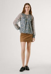 Blusa blu a maniche lunghe con scollatura arricciata, abbinata a una mini gonna in suede marrone e scarpe nere. Tessuto leggero e testurizzato.