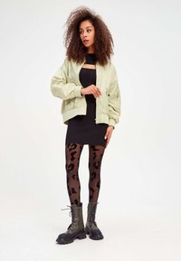 Veste bomber vert clair, robe noire côtelée, collants noirs transparents avec imprimé léopard et bottes de combat noires à semelles épaisses.