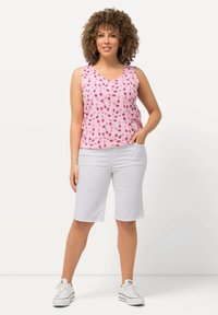 Top senza maniche rosa con un motivo di rossetti; abbinato a pantaloni corti bianchi fino al ginocchio e sneaker bianche. Look casual, vestibilità rilassata.