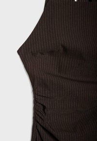 Kratak pogled na tamnosmeđi materijal s tankim bijelim prugicama u vertikalnom smjeru i nabiranim šavovima blizu bočne šavove na svijetloj pozadini.