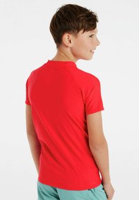 Raudona trumpa rankovėmis marškinėliai su apvaliu iškirpimu ir lygiu paviršiumi, prigludęs dizainas ir tiesus hem. Nėra matomų logotipų ar raštų.