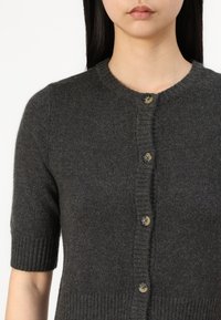 Cardigan court à manches courtes gris foncé en tricot doux, avec un col rond et cinq boutons ronds à l'avant.