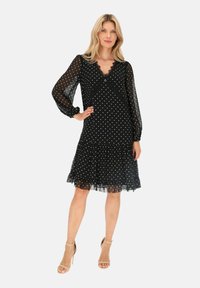 Czarna sukienka w kropki z przezroczystymi długimi rękawami, dekoltem w serek, koronkowym wykończeniem i falbaną u dołu. Lekki materiał i długość do kolan.
