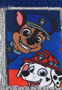 Un parche de personajes que presenta dos perros: uno marrón con un uniforme de policía azul y otro negro y blanco con un sombrero de bombero rojo sobre un fondo colorido.
