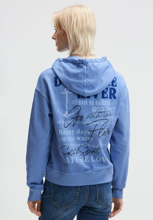 Blaue Kapuzenjacke mit Kordelzug, versehen mit strukturiertem Schriftzug und grafischem Design auf der Rückseite. Weiches Material, lockere Passform und gerippte Bündchen.
