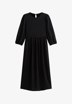 Vestido negro de mangas largas con un cuerpo texturizado, cintura fruncida y un detalle de abertura en la espalda. La falda fluida llega hasta la mitad de la pantorrilla.