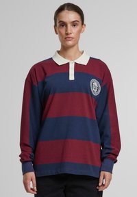 Dlhý rukáv polo tričko v maroon a námorníckych pruhov, so bielym golierom a kruhovým logom na ľavej hrudi. Bavlnená tkanina, voľný strih.