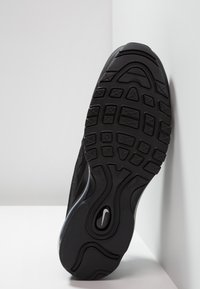 Suela de zapatilla deportiva negra con goma texturizada, que presenta un diseño ondulado y patrones de tracción multidireccional para agarre y estabilidad.