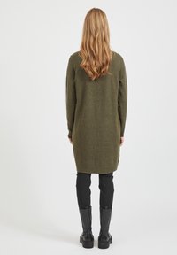 Lungo maglione verde oliva a maglia con polsini e orlo a coste, indossato sopra leggings neri e abbinato a stivali neri al ginocchio.