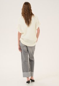 Knit cream top with short sleeves, paired with gray wide-leg jeans featuring a frayed cuff and relaxed fit, set against a plain background.