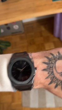 Zwart analoog horloge met een ronde wijzerplaat en een gestructureerde band. De wijzerplaat heeft minimalistische markeringen en een heldere glazen dekking.