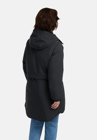 Zwarte pufferjas met een capuchon, verrimpelde taille en elastische boorden. Gladde textuur, knielange ontwerp met een subtiele glans.