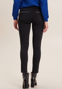 Jeans skinny noirs au toucher lisse, dotés de poches arrières zippées et d'un design ajusté, associés à des bottines noires à talons.