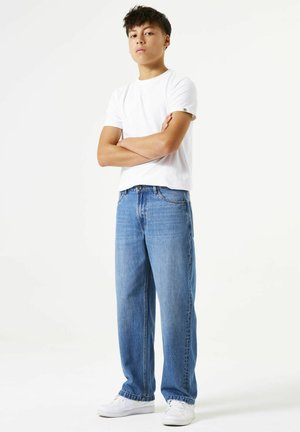 Weißes T-Shirt mit kurzen Ärmeln, kombiniert mit hellblauen Jeans mit geradem Bein. Weiße Turnschuhe. Minimalistisches Design, glatte Textur und legerer Schnitt.