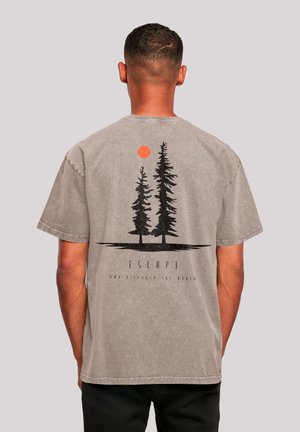 Mann von hinten, trägt ein graues T-Shirt mit schwarzen Baum-Silhouetten, einer orangefarbenen Sonne und den Texten "ESCAP" und "jetzt die Welt entdecken" auf der Rückseite.