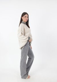 Suéter de punto crema de gran tamaño con cuello a rayas en blanco y negro, combinado con jeans grises de cintura alta. Textura suave y ajuste relajado.