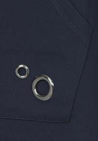 Marineblauer Stoff mit zwei metallischen Ösen, einer kleinen und einer größeren, mit glatter Textur und sichtbaren Nähten um eine Tasche.