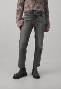 Jeans de mezclilla gris con corte recto, que cuentan con una cintura alta, bolsillos cosidos y un desvanecimiento sutil. Llevados con botas negras hasta el tobillo.