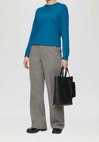 Turkusowy sweter z długim rękawem i okrągłym dekoltem, zestawiony z szarymi spodniami o szerokich nogawkach. Modelka trzyma czarną torebkę o teksturowanej powierzchni z małą sakwą.