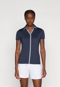 Námořnické polokošile s krátkým rukávem, bílým pruhovaným límcem a légou. Látka vypadá hladce a obtaženě, v kombinaci s bílými šortkami.