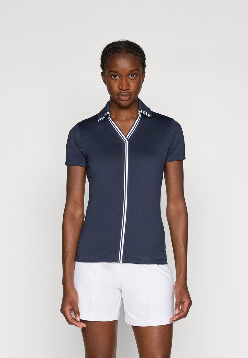 Námořnické polokošile s krátkým rukávem, bílým pruhovaným límcem a légou. Látka vypadá hladce a obtaženě, v kombinaci s bílými šortkami.