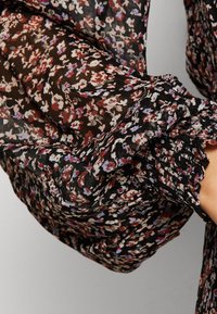 Schwarze, durchsichtige Bluse mit floralem Druck in Rot-, Weiß- und Violetttönen. Verfügt über Rüschenmanschetten und einen strukturierten Stoff, der sanft fällt.