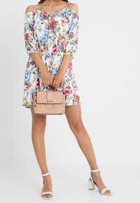 Šaty s květinovým vzorem, na ramínkách s volnými rukávy. Vytvořeno s malou strukturovanou béžovou kabelkou a bílými sandály na blokovém podpatku.