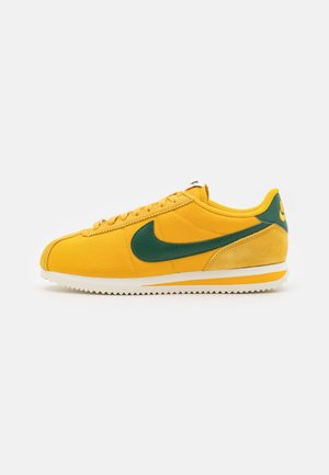 Baskets basses Nike jaunes et vertes avec un design à lacets et une semelle blanche rainurée, affichées sur un fond blanc.