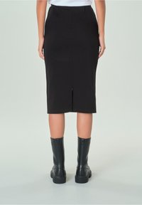 Falda lápiz negra con una abertura trasera, con una textura suave. Combinada con botas negras hasta la rodilla con suela gruesa.