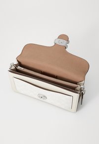 White leather handbag with a silver clasp, interior pocket, smooth finish, and a patterned front panel. Opened view showcasing inside texture.