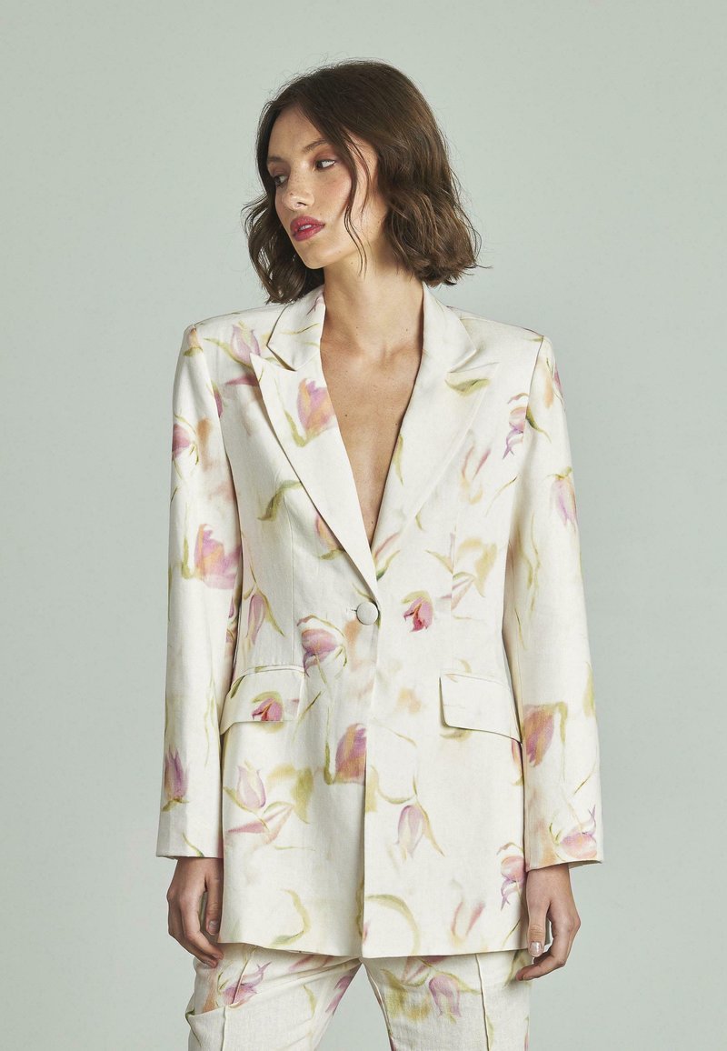 Blazer blanco con patrón floral en rosa y verde. Presenta un cuello con solapa, dos bolsillos frontales y un cierre de un solo botón. Textura suave.